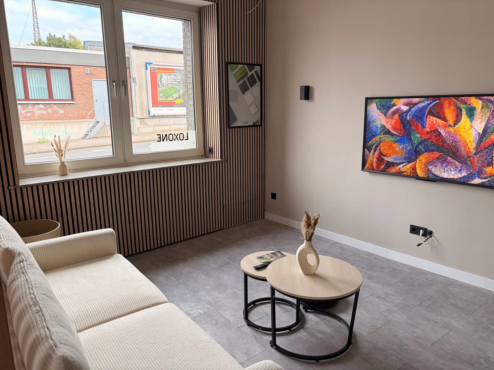 Wohnbereich im Showroom mit Sofa, Wandbild-Bildschirm und Loxone-Schriftzug am Fenster